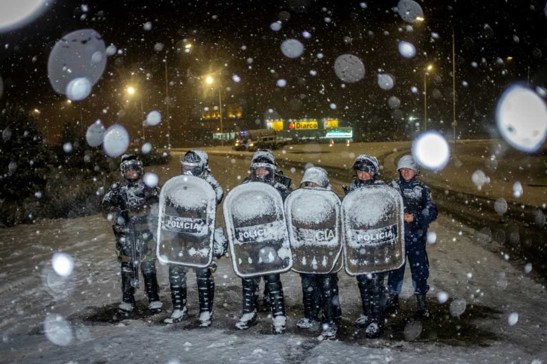 Police officers guard a Diarco supermarket under falling snow after an attempted looting