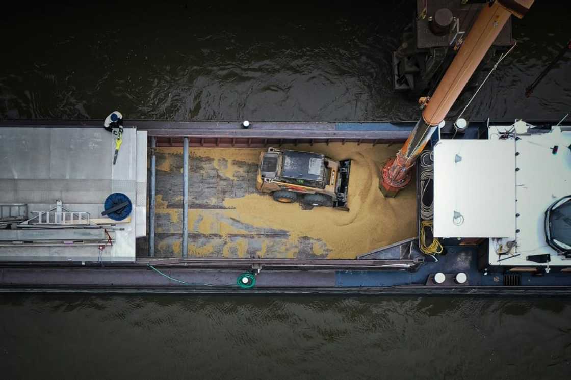 A tractor pushes grain toward a massive vacuum unloading a barge at the port A tractor pushes grain toward a massive vacuum unloading a barge at the port