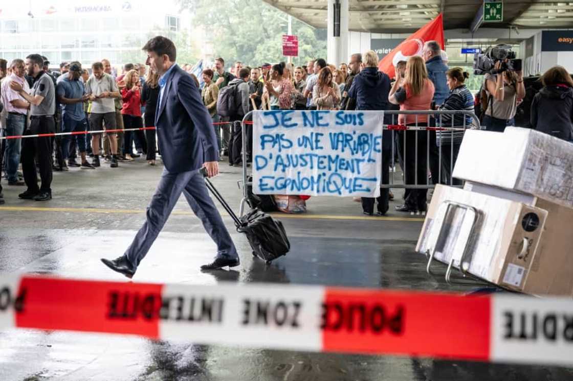 A traveller walks by a picket line where a sign reads 'I am not an economic adjustment variable'