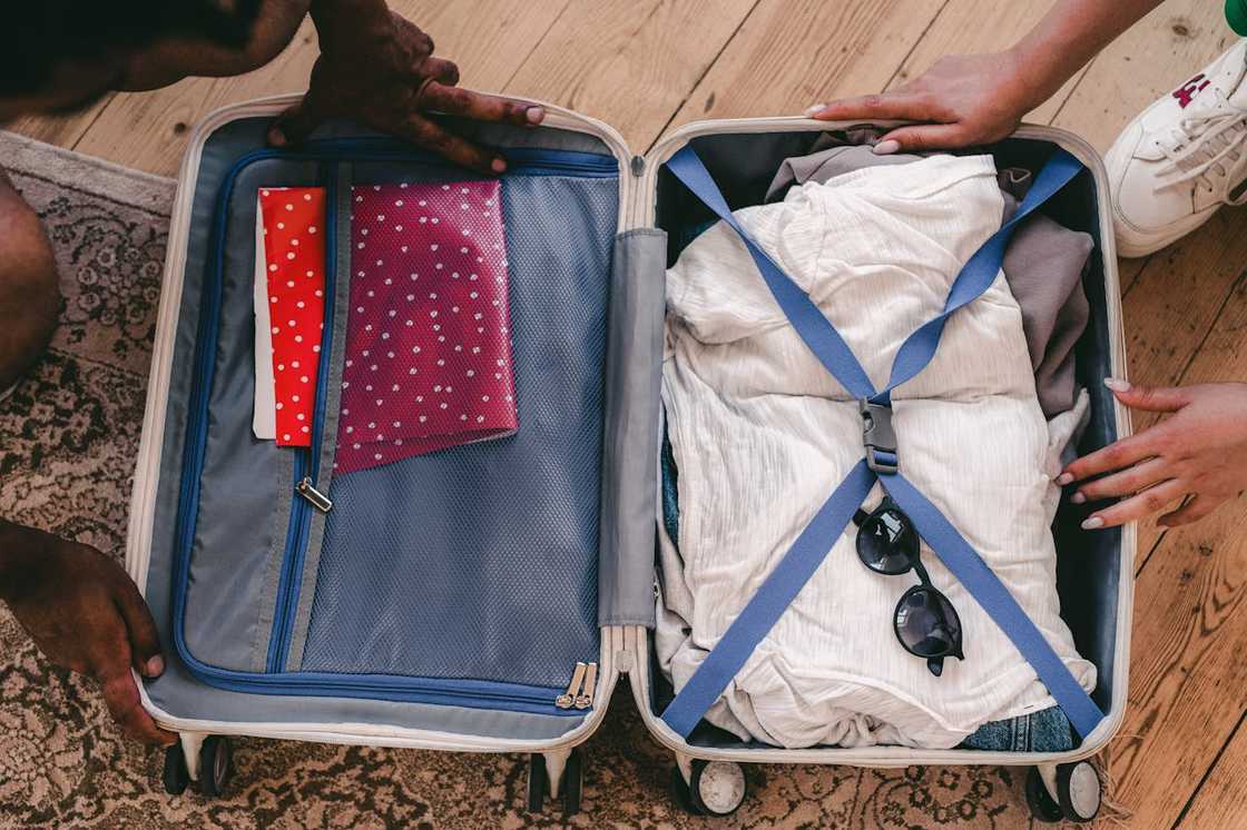 Hands pack clothes and accessories into an open suitcase.