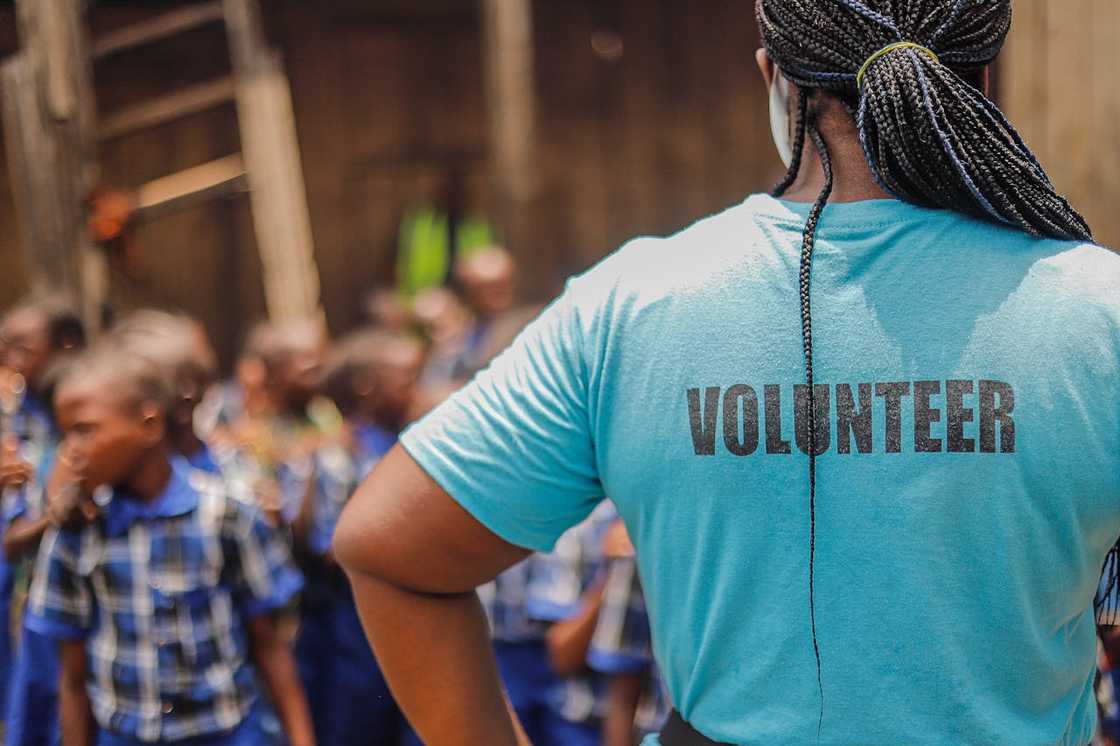 A volunteer stands facing a group of schoolchildren.