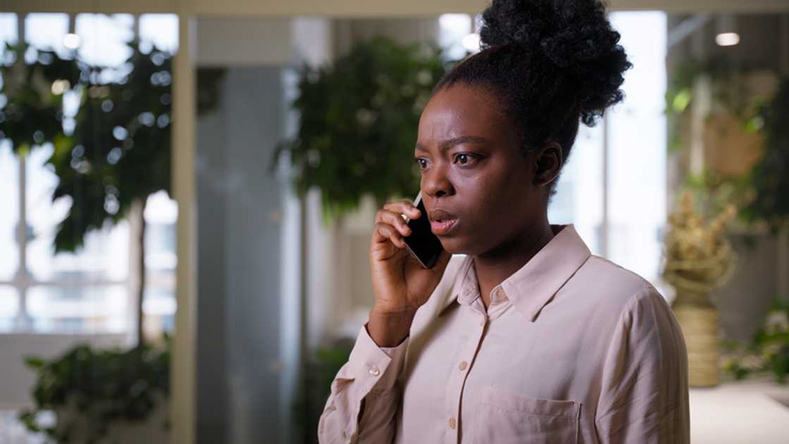 A woman speaks on the phone at her mansion at dusk.