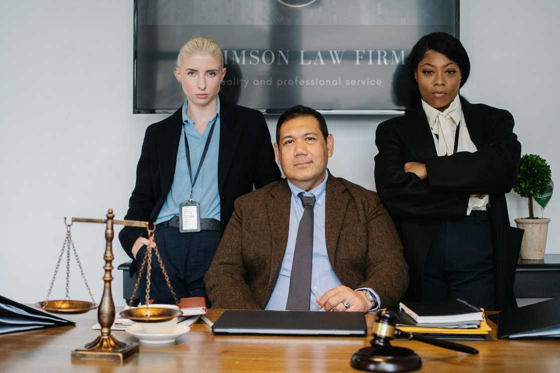 A team of three lawyers in suits stands in front of a table with a gavel