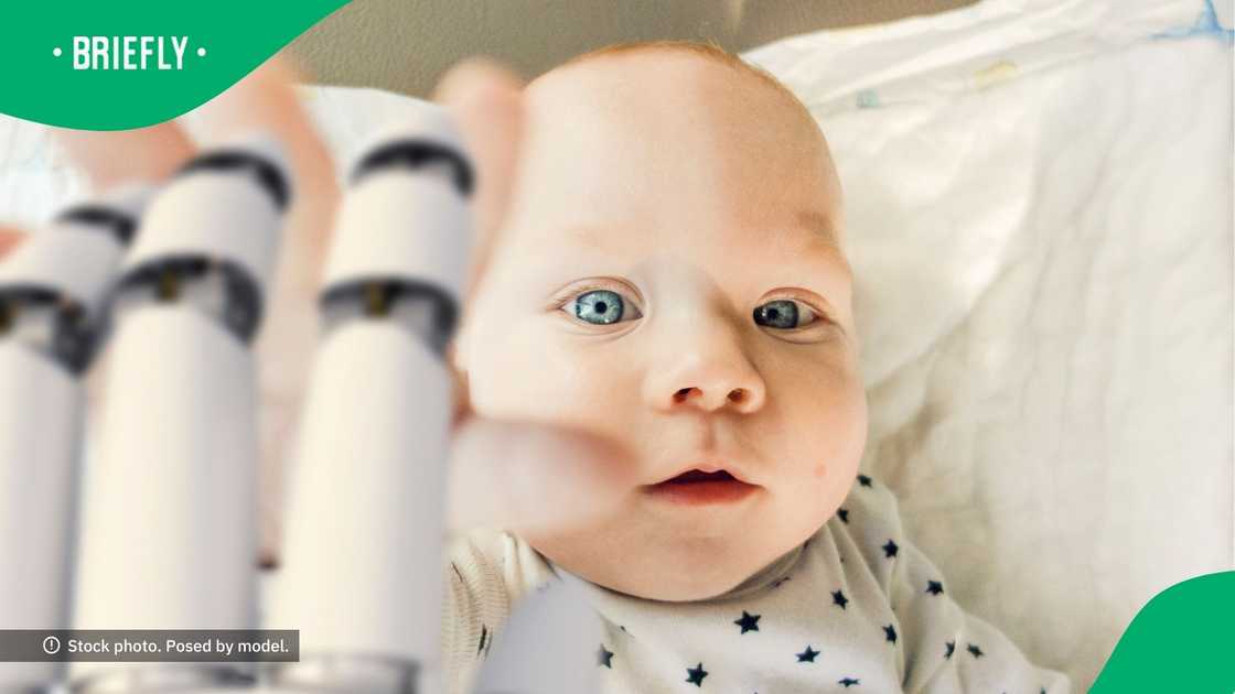 A baby reaching out to a robot's hand.