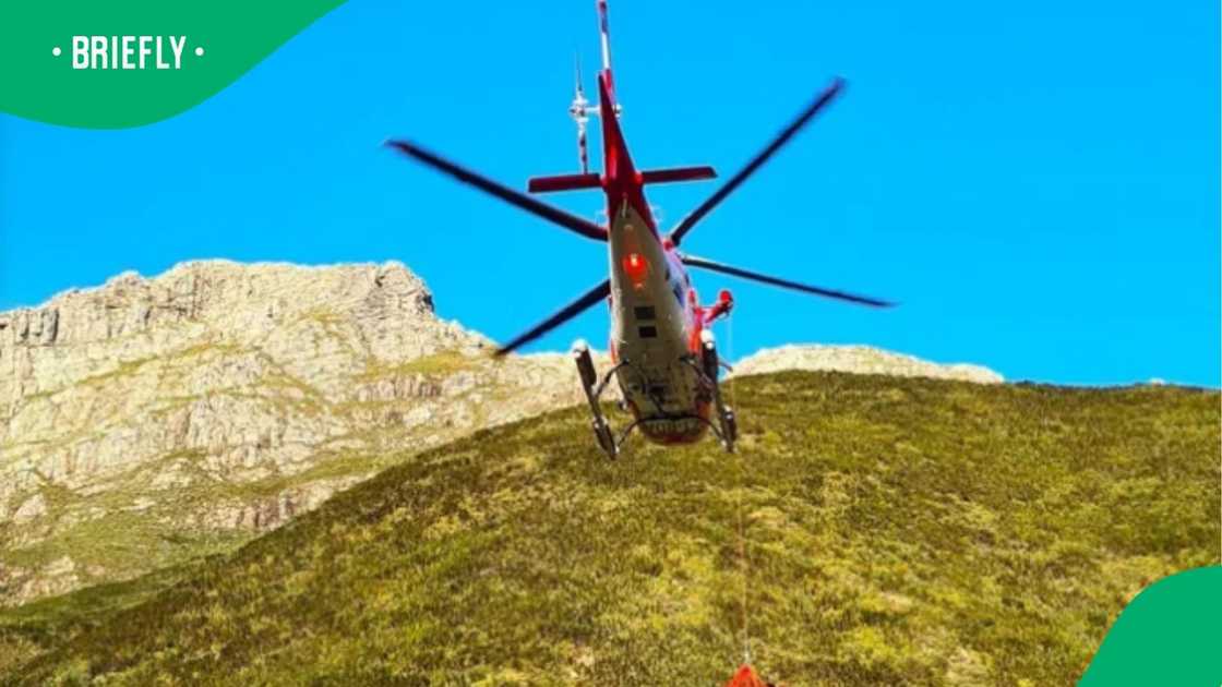 An emergency rescue helicopter hovered high in the air against a clear blue sky, preparing to airlift a fallen hiker from the rugged mountain terrain below An emergency rescue helicopter hovered high in the air against a clear blue sky, preparing to airlift a fallen hiker from the rugged mountain terrain below