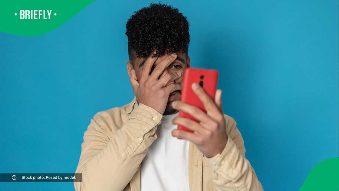 A man covering his face while looking at his phone. A man covering his face while looking at his phone.