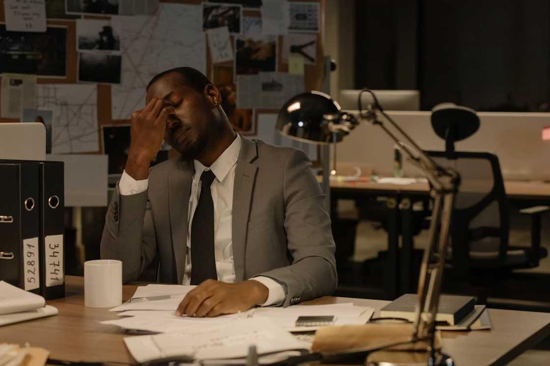A man in a suit sits at a desk, rubbing his forehead in frustration.