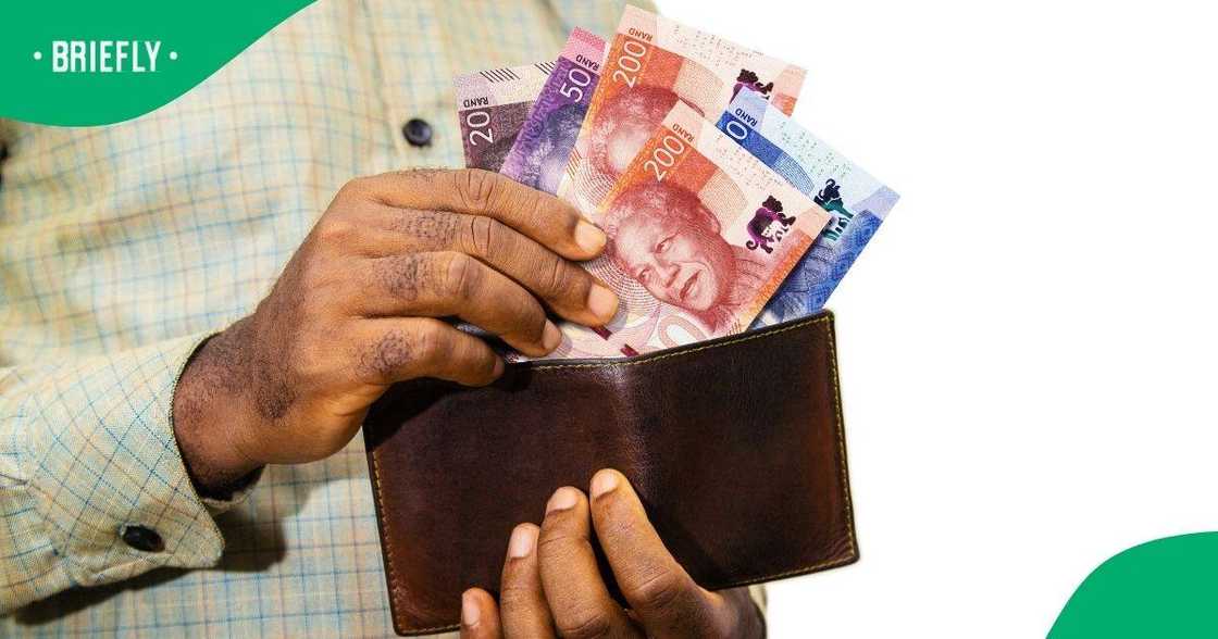 A man taking South African money out of his wallet.