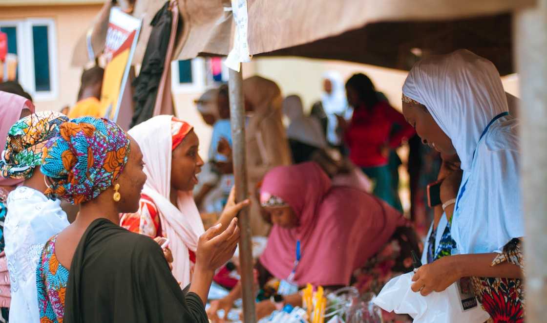 Several women wearing headscarves talk and trade items at a busy outdoor market. Several women wearing headscarves talk and trade items at a busy outdoor market.