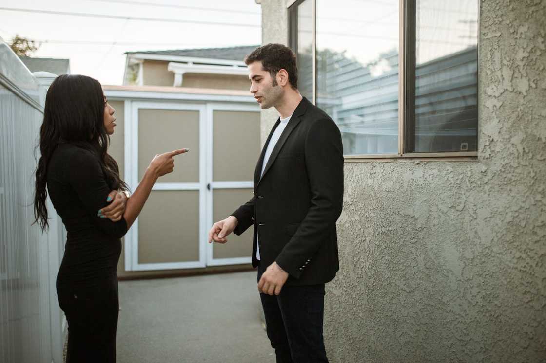 A woman points while arguing with a man outside a house.