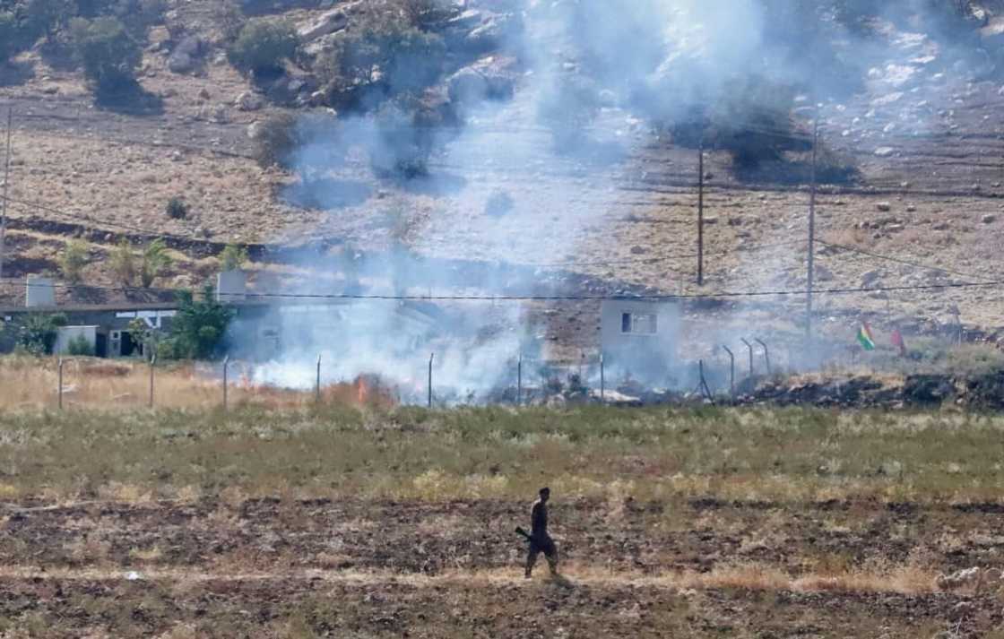 A Kurdish peshmerga fighter walks as smoke billows in the area of Zargwez, outside the Iraqi city of Sulaimaniyah, where several exiled left-wing Iranian Kurdish parties maintain offices