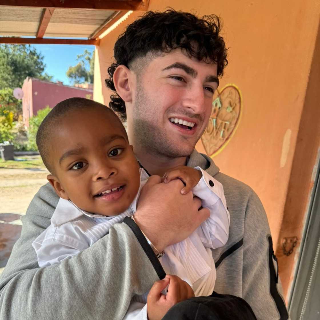 Man in a grey jacket hugs a small child in white clothing outside a building Man in a grey jacket hugs a small child in white clothing outside a building