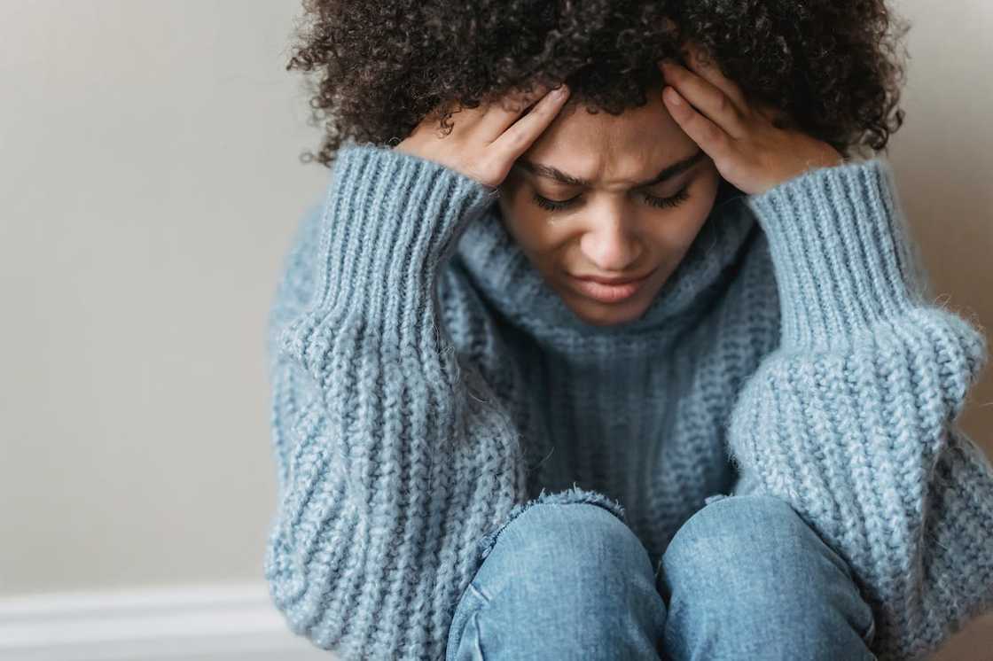 A woman sits on the floor holding her head in distress.