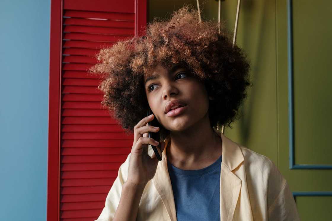 A young woman with curly hair talking on her mobile phone indoors.