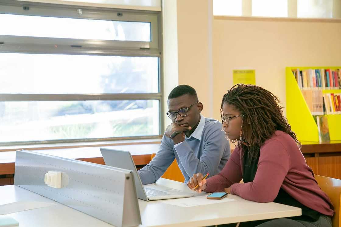 Two students in glasses working together using one laptop Two students in glasses working together using one laptop