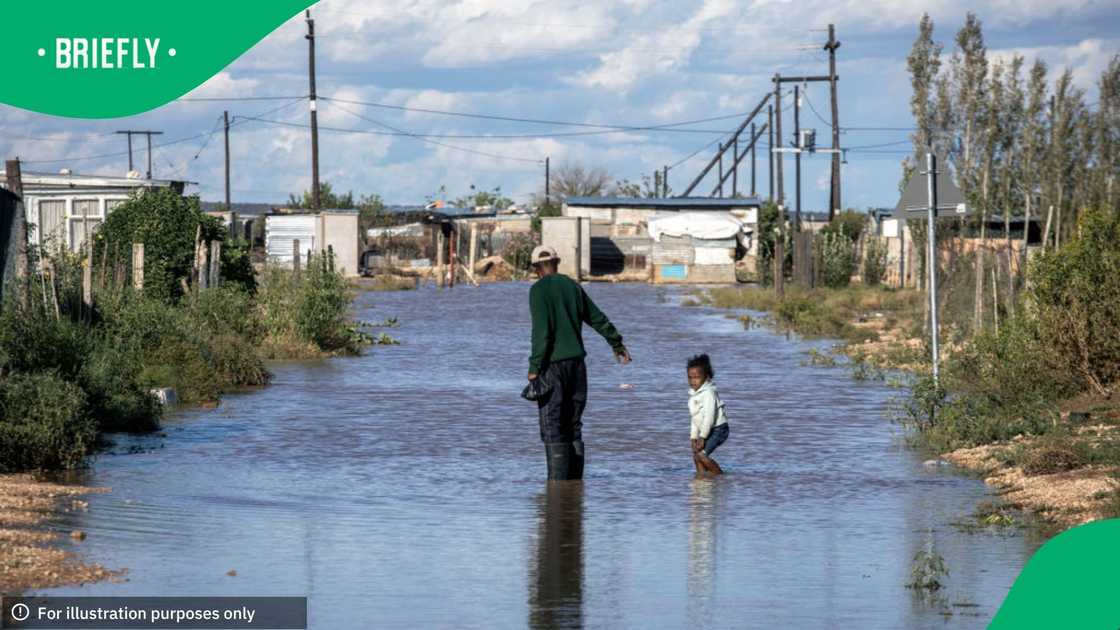 A man walks with his granddaughter in the water after severe rains hit Snake Park, an informal settlement on April 8, 2024, outside Hope Town, Northern Cape Province, South Africa