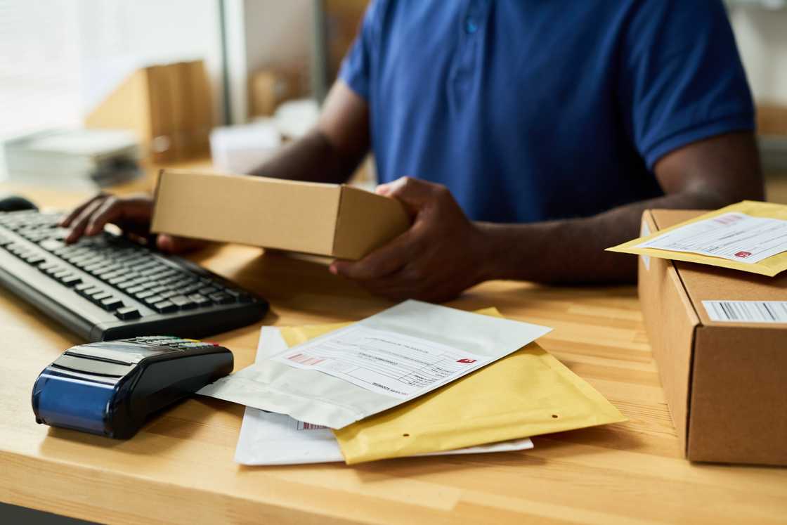 A person holds a small cardboard package while working at a desk.
