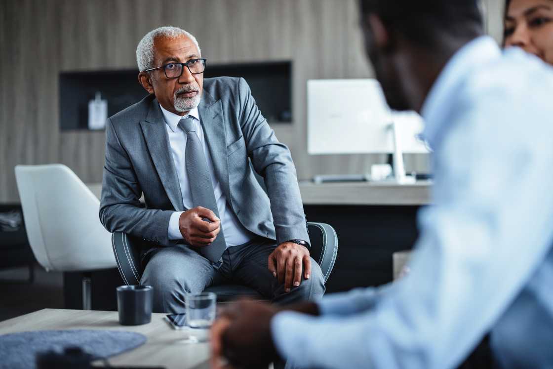 An older man confronts a lawyer in an office under a ceiling fan.