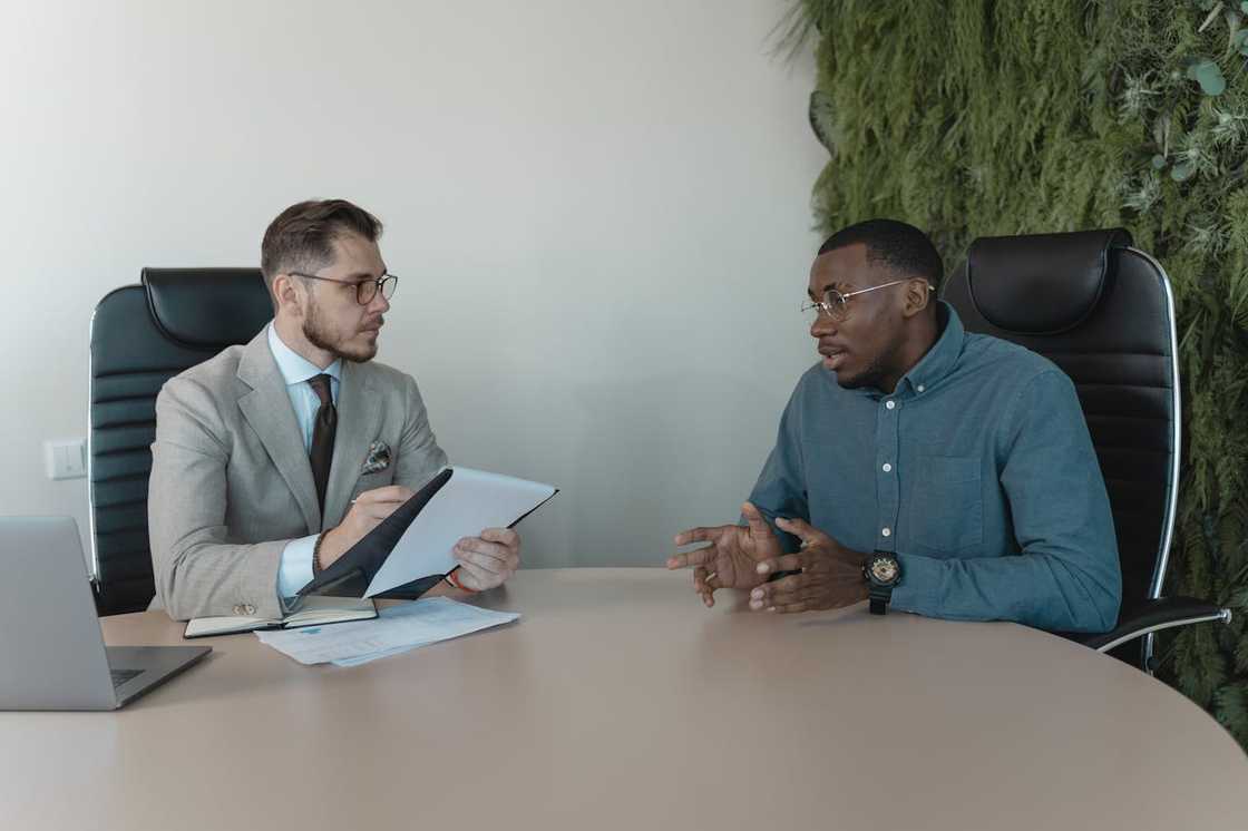 Two men in a serious conversation across a desk in an office setting. Two men in a serious conversation across a desk in an office setting.