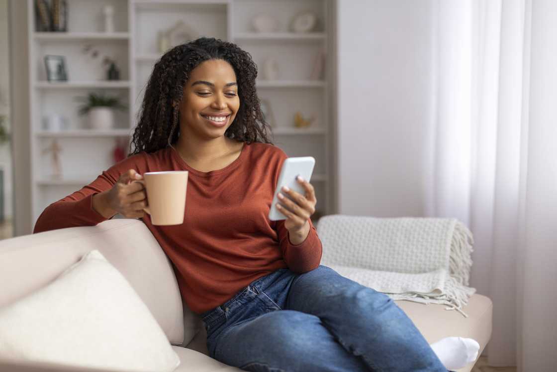 A woman with a mug in the one hand and her phone in the other.