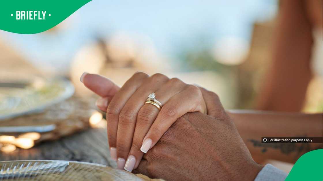 Bride with wedding ring holding hand of groom at table in winery