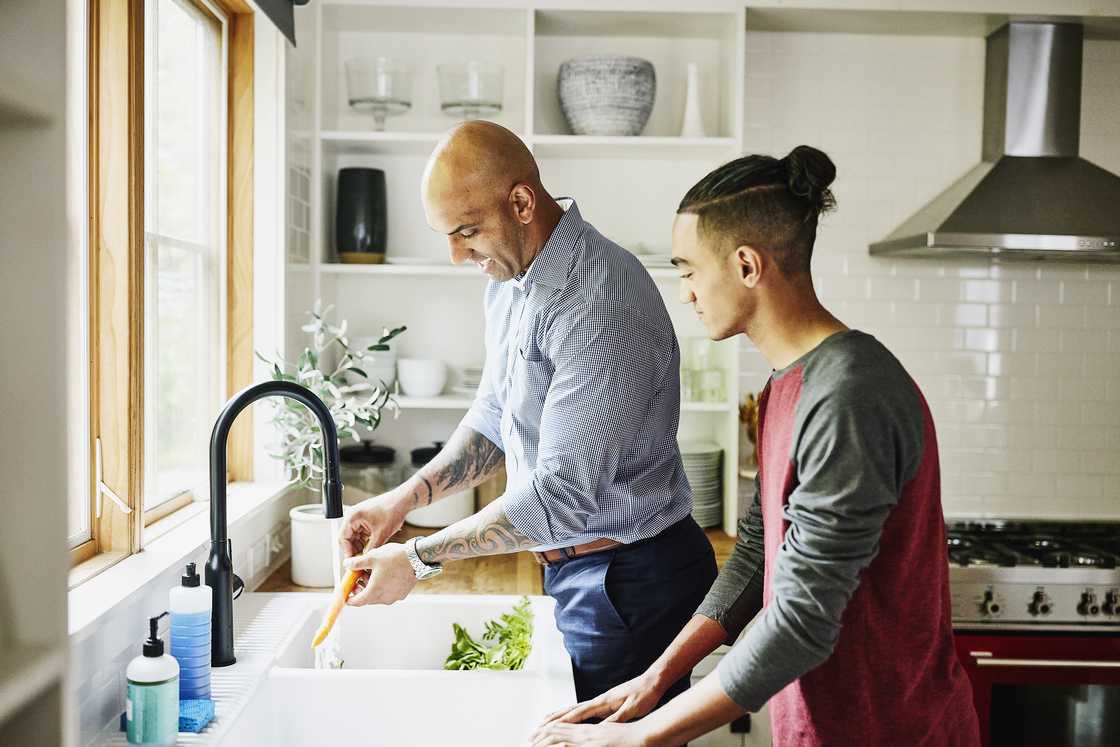 Father and son washing vegetables in kitchen sink