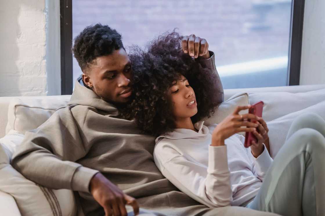 A couple relaxes on a couch looking at a phone.