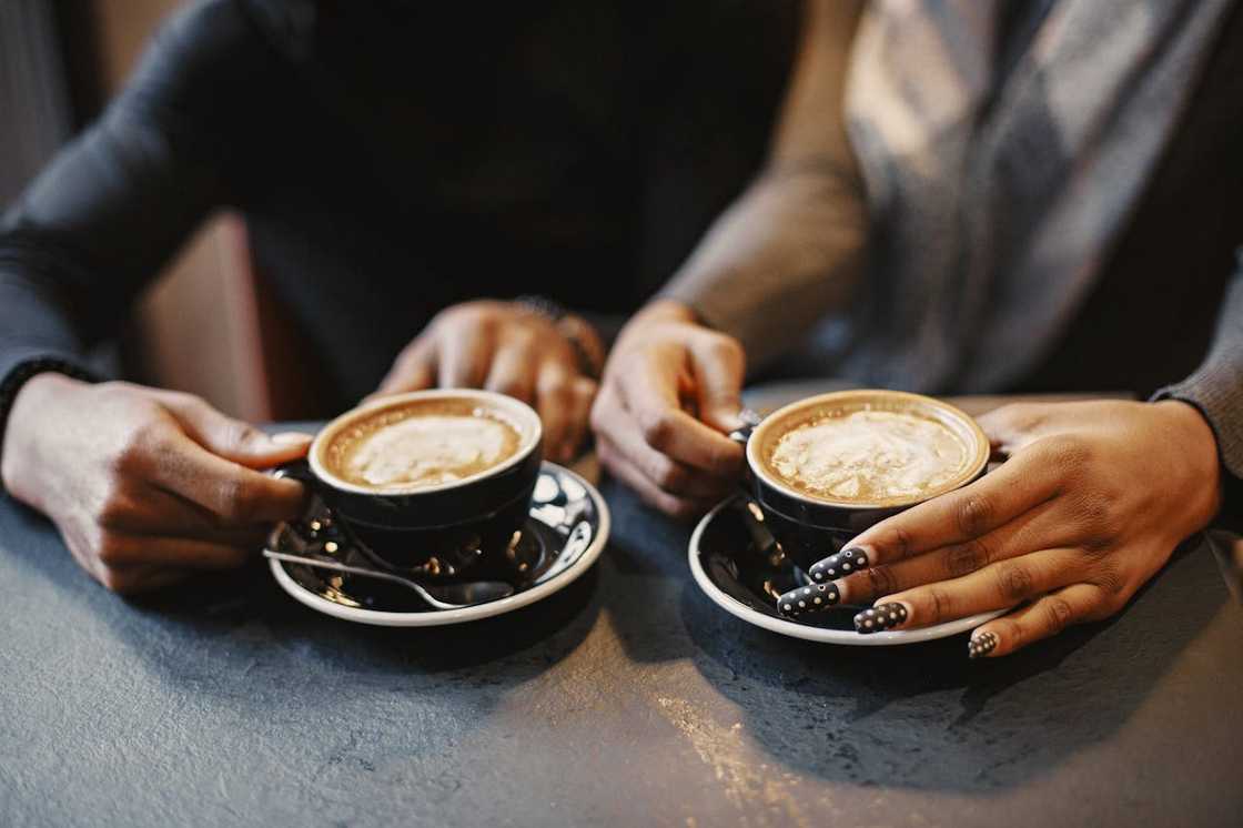 Two people sitting at a café table, each holding a cup of coffee in black saucers.