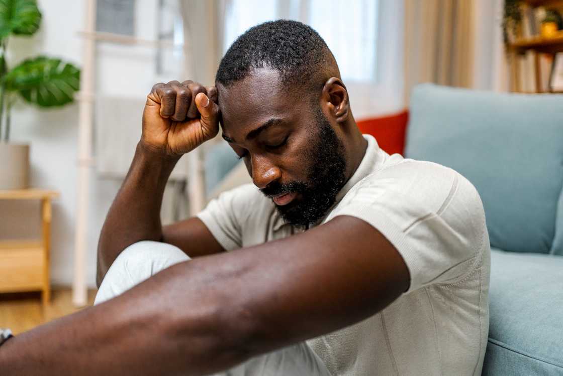 A worried man sitting alone on the floor in a living room
