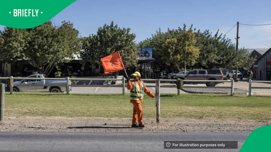A worker from the South African National Roads Agency SOC Ltd (SANRAL) flags down passing motorists as a team cuts grass outside Orania, on May 27, 2024 A worker from the South African National Roads Agency SOC Ltd (SANRAL) flags down passing motorists as a team cuts grass outside Orania, on May 27, 2024