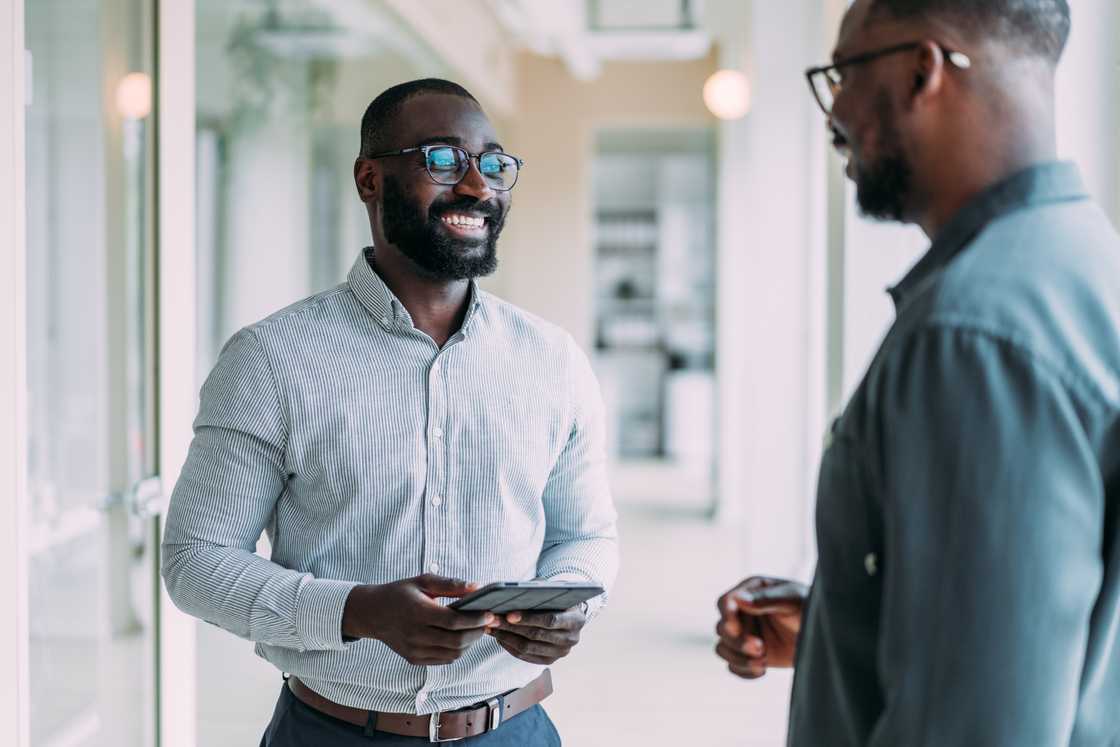 two employees chatting in the office smiling two employees chatting in the office smiling
