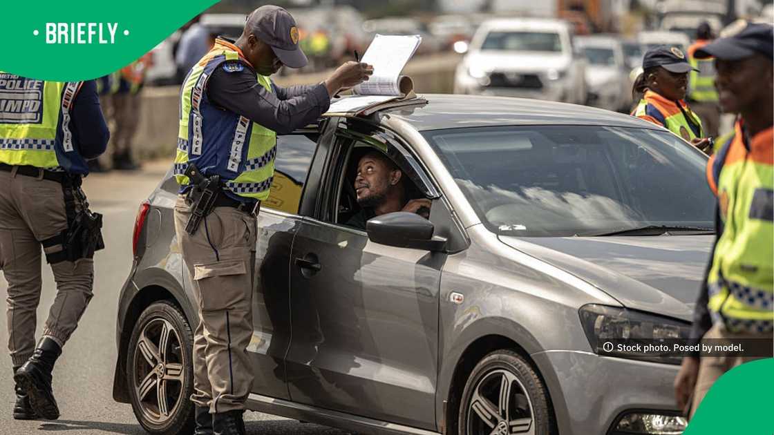 Several law enforcement officers in high-visibility vests conducted a routine traffic stop on a busy road filled with vehicles in the background