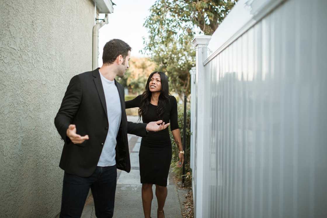 A man and woman argue while walking through a narrow outdoor passage.