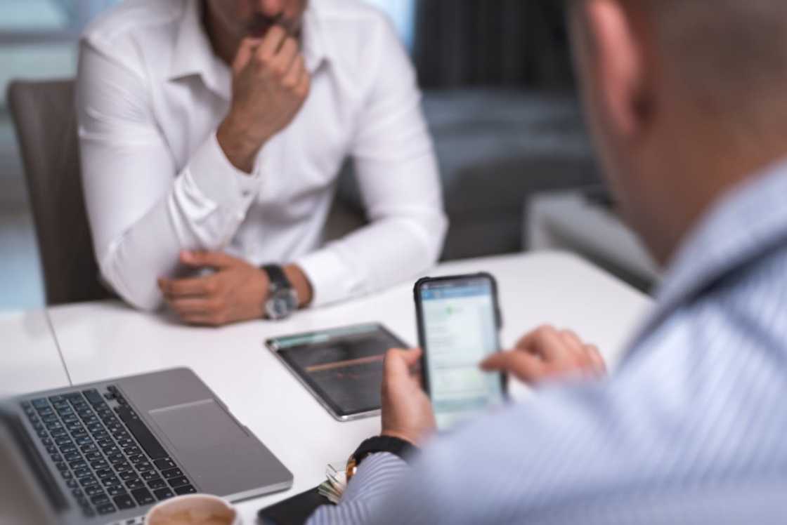 A man looks at a phone while another man sits across the table. A man looks at a phone while another man sits across the table.