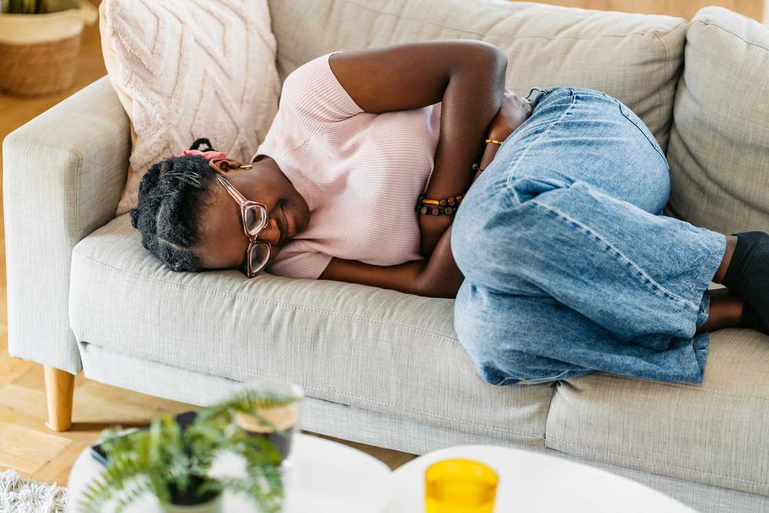 Young black woman lying on the sofa and having period cramps. Close-up.