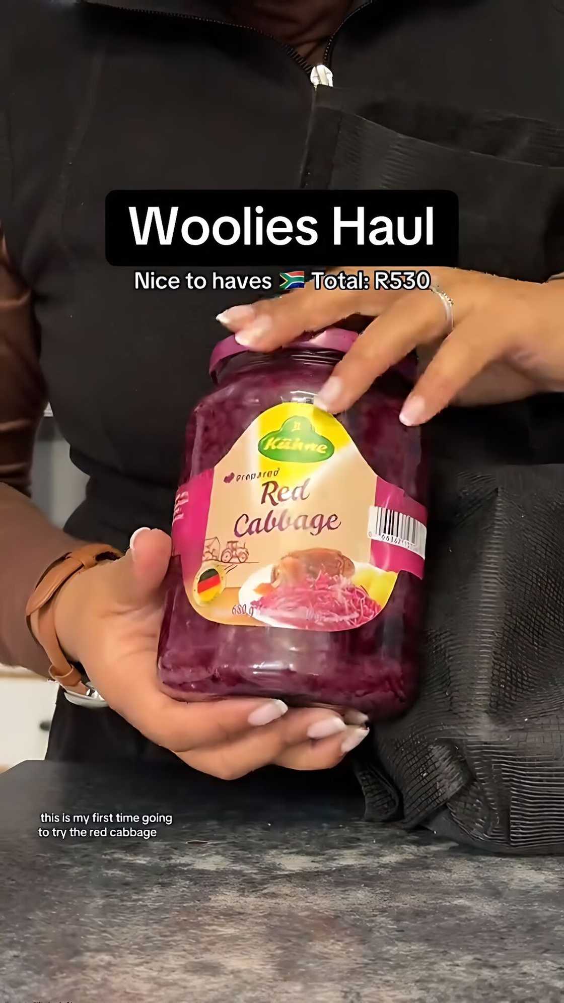 Hands holding a jar of Kühne prepared red cabbage from a Woolworths grocery haul, shown against a dark bag. Hands holding a jar of Kühne prepared red cabbage from a Woolworths grocery haul, shown against a dark bag.