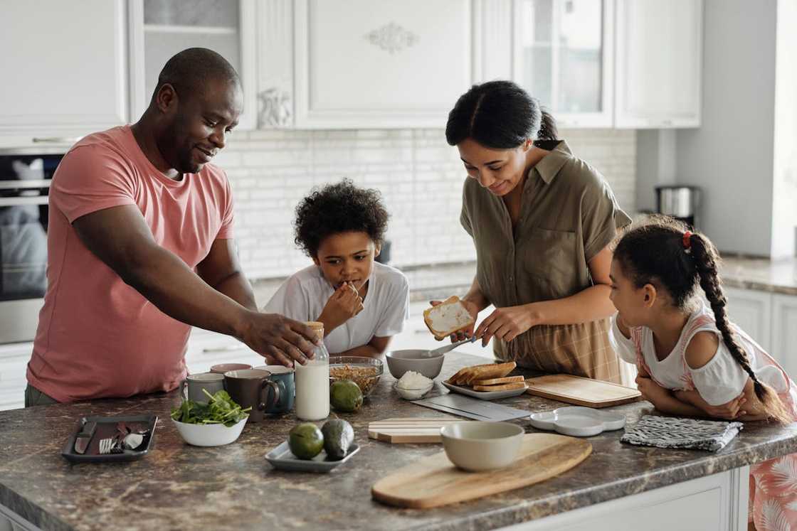 A family stands around a kitchen counter preparing food together.
