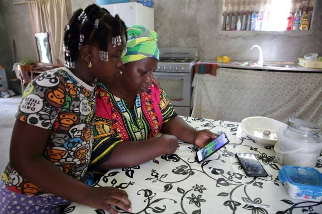 Elsy Poeketie shows her granddaughter images of her flooded holiday resort at the Moedjecreek Nieuw Lombe village in Suriname