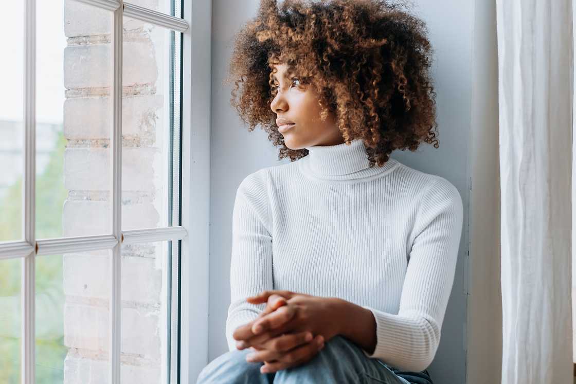 A woman sits on a white windowsill looking outside