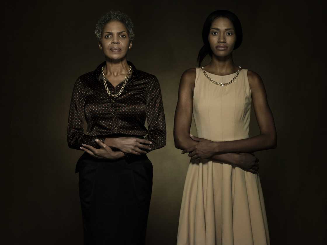 Two individuals stand side by side with arms crossed against a dark background. Two individuals stand side by side with arms crossed against a dark background.