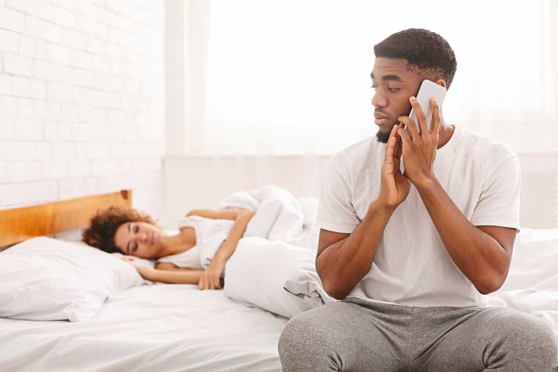 A man on the phone at bedside while partner sleeps. A man on the phone at bedside while partner sleeps.