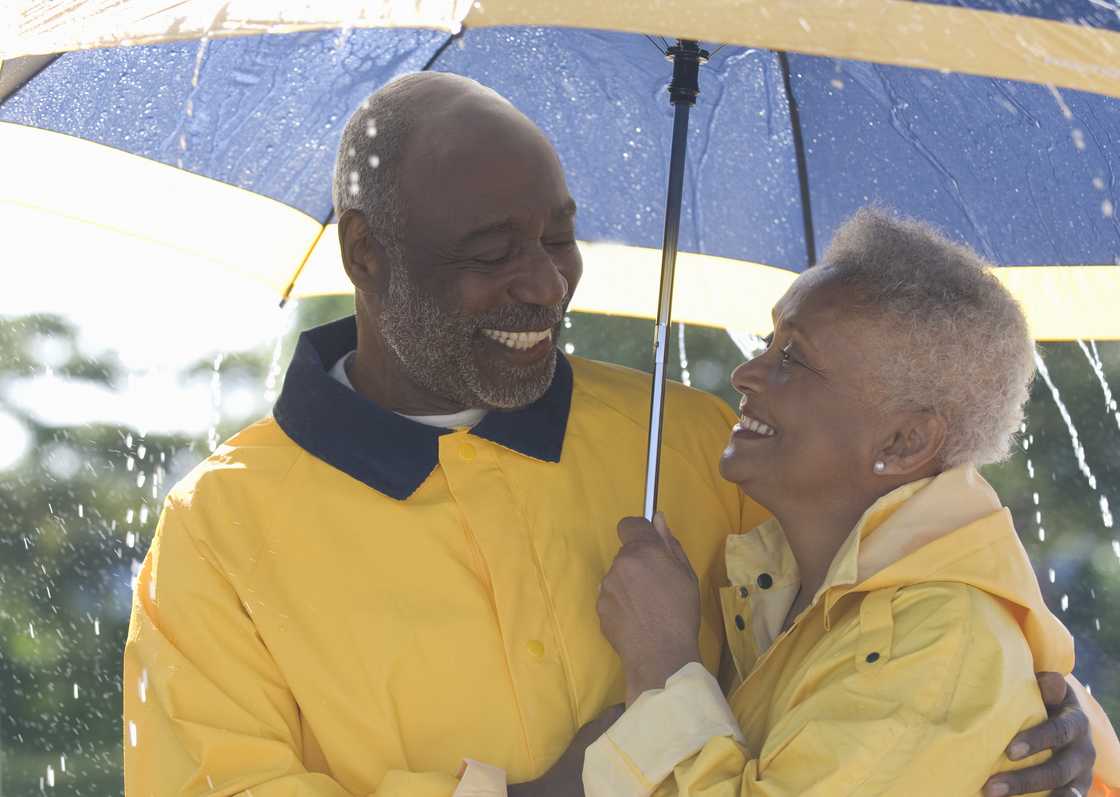 Elderly couple under an umbrella and standing in the rain.