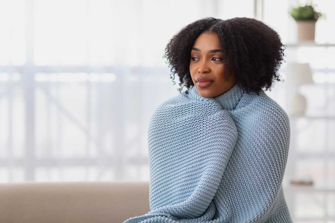 A woman with curly hair wrapped snugly in a blue knitted blanket A woman with curly hair wrapped snugly in a blue knitted blanket