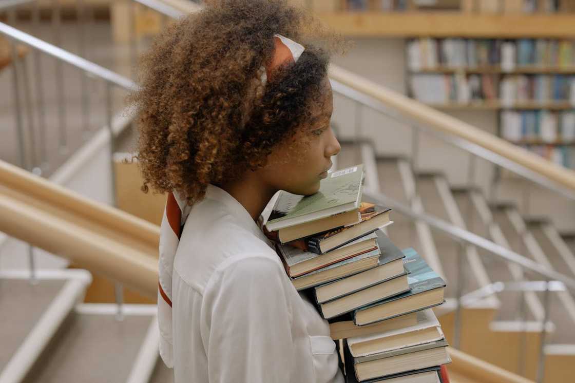 A young woman carrying a tall stack of books. A young woman carrying a tall stack of books.