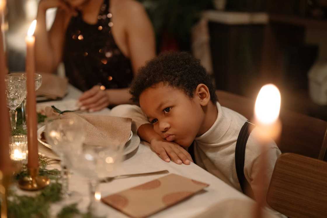 A young boy rests his head on a table during a candlelit dinner.