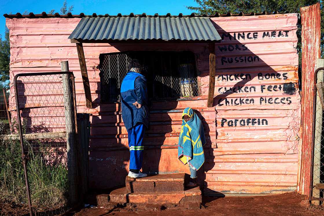 A man and a child shop at a local spaza shop in an informal settlement on May 6, 2026 in Mountain City south of Johannesburg, South Africa