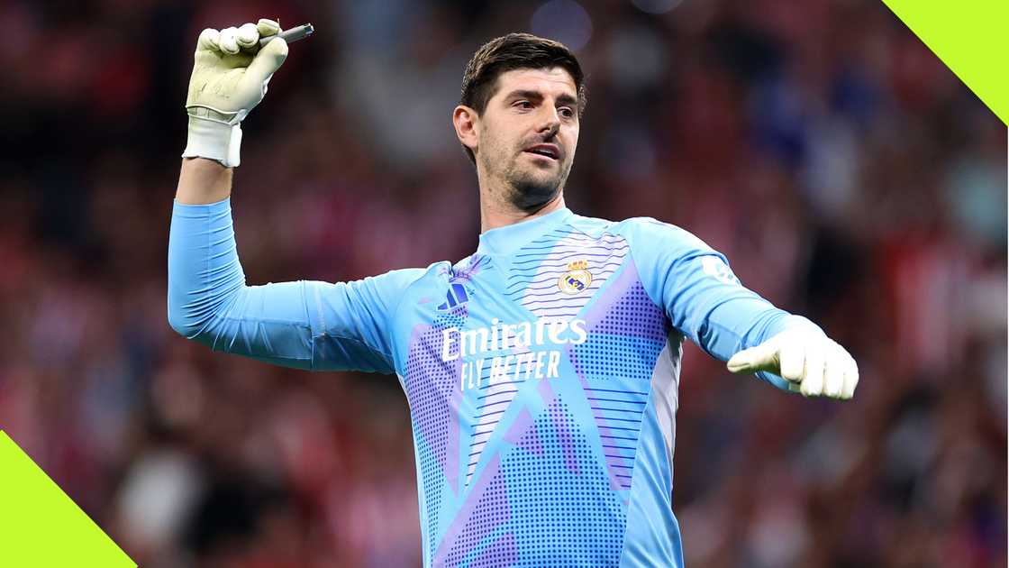 Real Madrid goalkeeper Thibaut Courtois throwing back an object hurled at him by Atletico Madrid fans behind his goalpost.