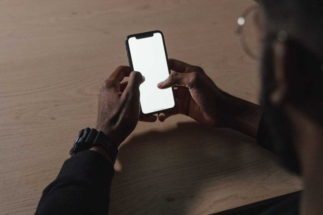 A person holds a smartphone with a blank screen while sitting at a table.