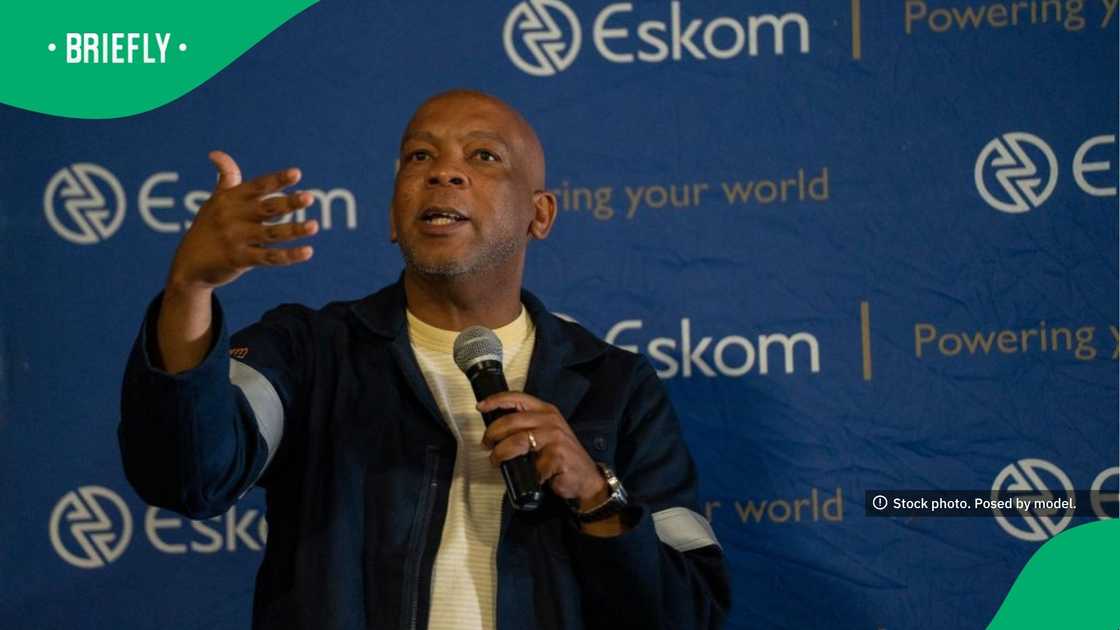 Standing before a blue Eskom backdrop, the minister addressed workers while holding a microphone and wearing a dark jacket