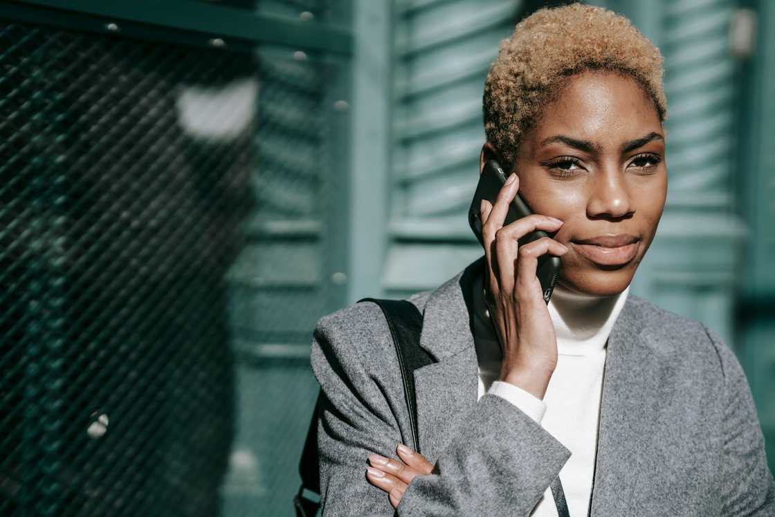 A woman in a grey jacket and dyed short hair makes a phone call